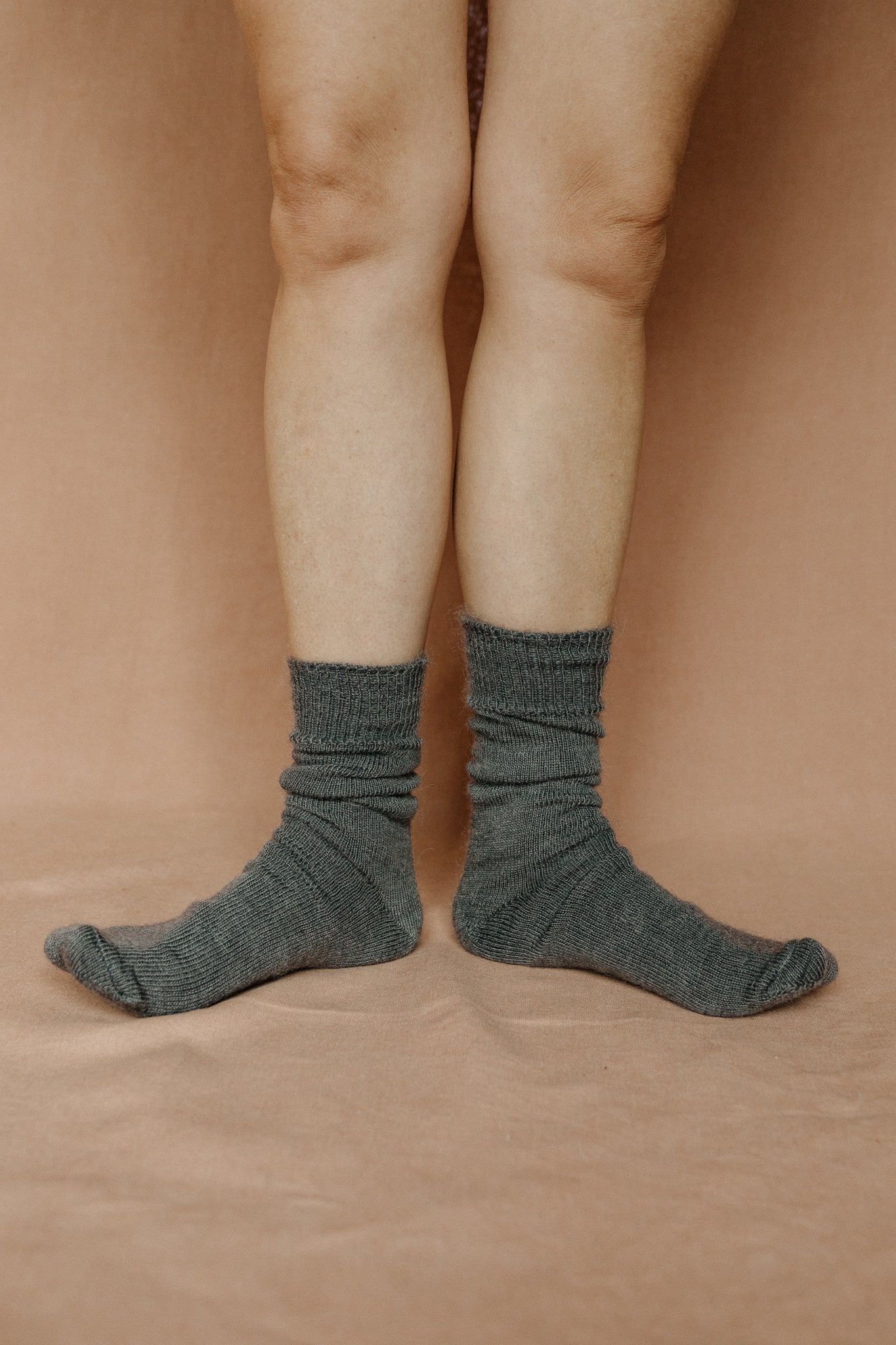 Image of someone wearing grey mohair socks with bare legs against a terracotta background.