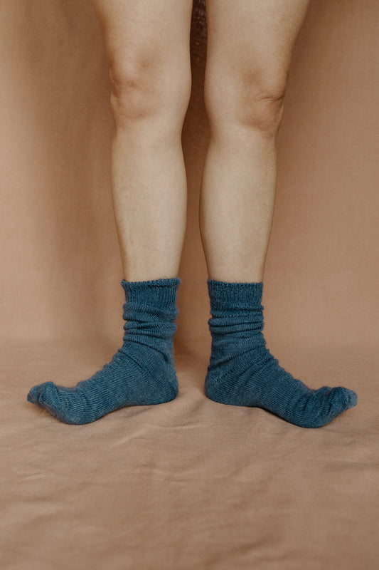 Image of someone wearing dark blue mohair socks with bare legs against a terracotta background.
