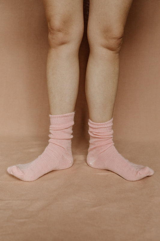 Image of someone wearing light pink mohair socks with bare legs against a terracotta background.