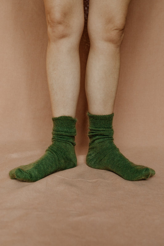 Image of someone wearing green mohair socks with bare legs against a terracotta background.