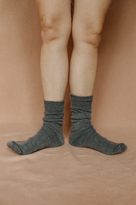 Image of someone wearing grey mohair socks with bare legs against a terracotta background.