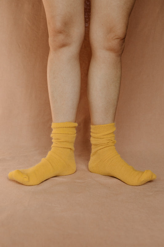 Image of someone wearing yellow mohair socks with bare legs against a terracotta background.