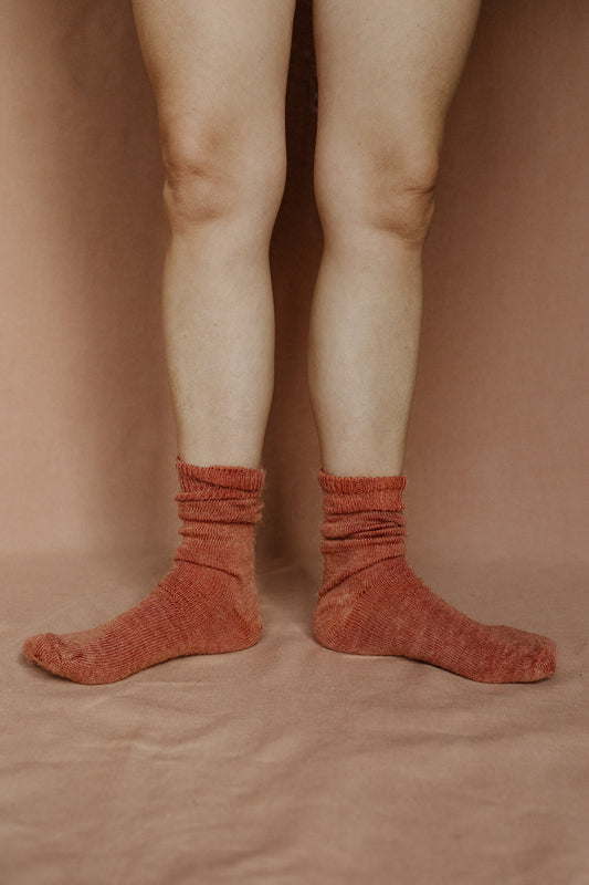 Image of someone wearing rust coloured mohair socks with bare legs against a terracotta background.